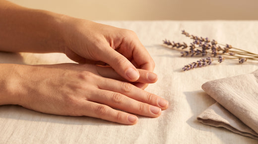 Mãos a massajar as unhas naturais sobre linho creme com lavanda seca